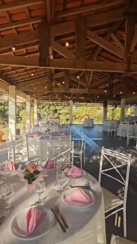 Mesas postas com guardanapos rosa sob a pérgola de uma chácara